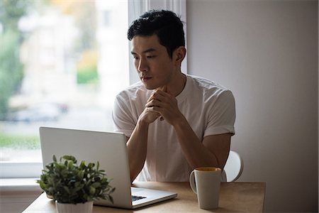 simsearch:6109-08804908,k - Man looking at laptop with a cup of coffee on table at home Photographie de stock - Premium Libres de Droits, Code: 6109-08804968