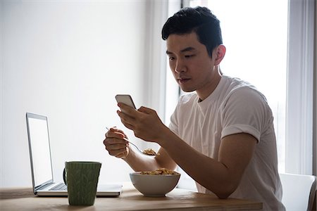 simsearch:6108-07969489,k - Man using mobile phone while having breakfast at home Foto de stock - Sin royalties Premium, Código: 6109-08804973