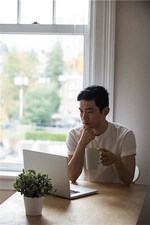 simsearch:6109-08804908,k - Man looking at laptop while having a cup of coffee at home Photographie de stock - Premium Libres de Droits, Code: 6109-08804970