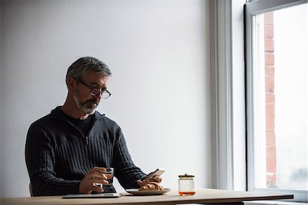 simsearch:6109-08804993,k - Man using mobile phone while having a glass of water at home Fotografie stock - Premium Royalty-Free, Codice: 6109-08804995