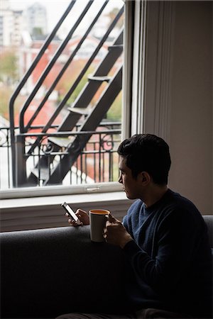 simsearch:6109-08804993,k - Man using mobilephone while having a cup of coffee at home Fotografie stock - Premium Royalty-Free, Codice: 6109-08804904