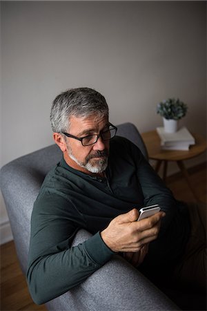 Man using mobile phone in living room at home Stock Photo - Premium Royalty-Free, Code: 6109-08805022