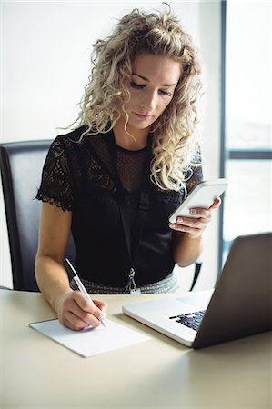 simsearch:6109-08829578,k - Businesswoman writing on notepad while using mobile phone Stock Photo - Premium Royalty-Free, Code: 6109-08829567