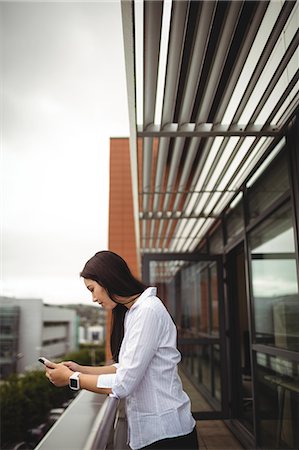 simsearch:6109-08829578,k - Businesswoman using mobile phone at office balcony Stock Photo - Premium Royalty-Free, Code: 6109-08829704