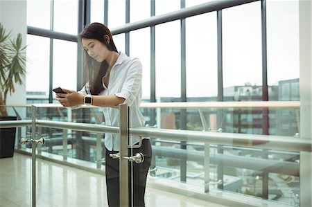 simsearch:6109-08829578,k - Businesswoman leaning on railing and using mobile phone Stock Photo - Premium Royalty-Free, Code: 6109-08829721
