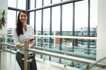 simsearch:6109-08829709,k - Smiling businesswoman holding mobile phone in office corridor Stock Photo - Premium Royalty-Free, Code: 6109-08829722