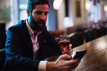 Businessman using mobile phone with glass of red wine in hand Stock Photo - Premium Royalty-Free, Code: 6109-08829860