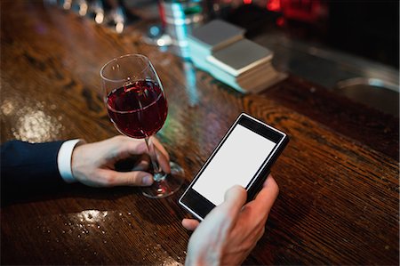 Businessman using mobile phone with glass of red wine in hand Stock Photo - Premium Royalty-Free, Code: 6109-08829864