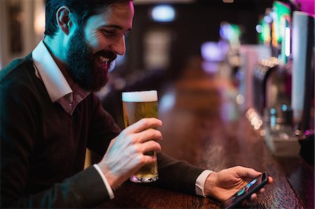 restaurant bar counters - Man looking at mobile phone while having glass of beer Stock Photo - Premium Royalty-Free, Code: 6109-08829873