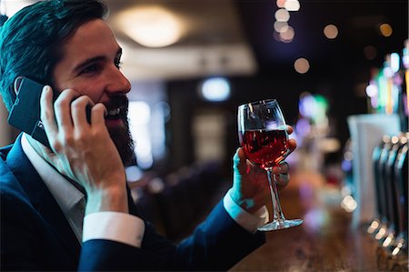 Businessman talking on mobile phone while having glass of wine Stock Photo - Premium Royalty-Free, Code: 6109-08829884