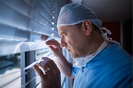 simsearch:400-07334526,k - Surgeon looking through window blind at hospital Photographie de stock - Premium Libres de Droits, Code: 6109-08829986