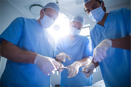 simsearch:6109-08830118,k - Group of surgeons performing operation in operation room Foto de stock - Sin royalties Premium, Código: 6109-08829998