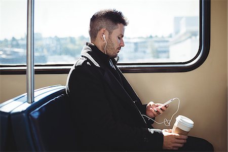 simsearch:6109-08700193,k - Businessman holding a disposable coffee cup and listening to music on mobile phone Stock Photo - Premium Royalty-Free, Code: 6109-08830063