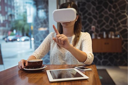 simsearch:6109-08830087,k - Businesswoman using vr headset while sitting at table with coffee, digital tablet and phone Stock Photo - Premium Royalty-Free, Code: 6109-08830098