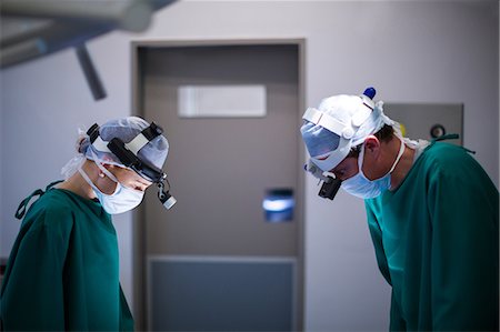 simsearch:6109-08830118,k - Surgeons wearing surgical loupes while performing operation Foto de stock - Sin royalties Premium, Código: 6109-08830145