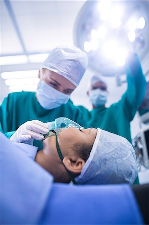 simsearch:6109-08689539,k - Surgeon adjusting oxygen mask on patient mouth in operation theater Stock Photo - Premium Royalty-Free, Code: 6109-08830114