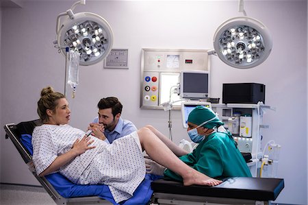 simsearch:6109-08830452,k - Doctor examining pregnant woman during delivery while man holding her hand in operating room Stock Photo - Premium Royalty-Free, Code: 6109-08830572