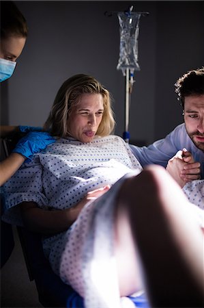 simsearch:6109-08830575,k - Doctor examining pregnant woman during delivery while man holding her hand in operating room Stock Photo - Premium Royalty-Free, Code: 6109-08830577