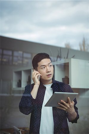 simsearch:6109-08830034,k - Business executive talking on mobile phone while using digital tablet Fotografie stock - Premium Royalty-Free, Codice: 6109-08830763