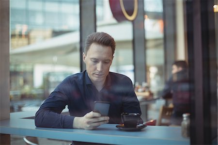 Male executive using mobile phone at counter in cafeteria Stock Photo - Premium Royalty-Free, Code: 6109-08944254