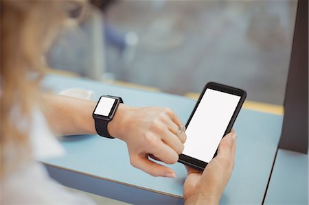 simsearch:6109-08944310,k - Woman using mobile and checking time at counter in cafeteria Photographie de stock - Premium Libres de Droits, Code: 6109-08944310