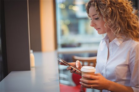 simsearch:6109-07496970,k - Woman using mobile phone while having coffee at counter in cafeteria Fotografie stock - Premium Royalty-Free, Codice: 6109-08944338