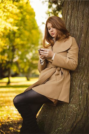 simsearch:6109-08944833,k - Beautiful woman using mobile phone while standing in the park Photographie de stock - Premium Libres de Droits, Code: 6109-08944442