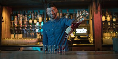 simsearch:6109-08944480,k - Bartender pouring alcoholic drink in shot glasses at bar Fotografie stock - Premium Royalty-Free, Codice: 6109-08944467