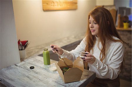 simsearch:649-06352854,k - Woman holding mobile phone while eating in the restaurant Stock Photo - Premium Royalty-Free, Code: 6109-08944407