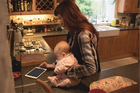 simsearch:6109-08944723,k - Mother using digital tablet while carrying her baby in kitchen at home Stock Photo - Premium Royalty-Free, Code: 6109-08944562