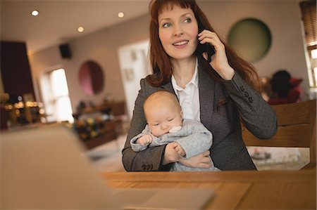 Mother talking on mobile phone while holding her baby at home Stock Photo - Premium Royalty-Free, Code: 6109-08944577