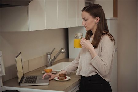Woman using laptop while having breakfast in kitchen at home Stock Photo - Premium Royalty-Free, Code: 6109-08944599