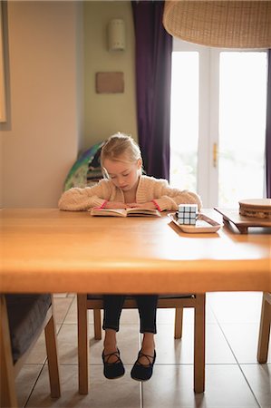 Cute girl sitting at table and reading book at home Stock Photo - Premium Royalty-Free, Code: 6109-08944527