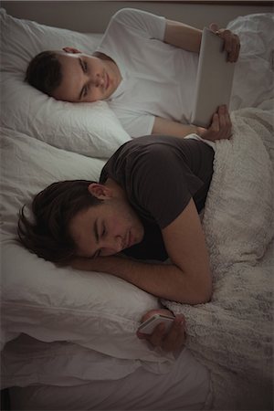 simsearch:6109-08944593,k - Gay couple using mobile phone and digital tablet while lying on bed in bedroom Stock Photo - Premium Royalty-Free, Code: 6109-08944650