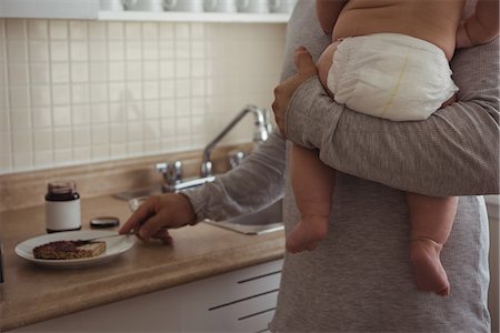 father baby boy diaper - Mid section of father preparing breakfast while holding his baby in kitchen Stock Photo - Premium Royalty-Free, Code: 6109-08944671