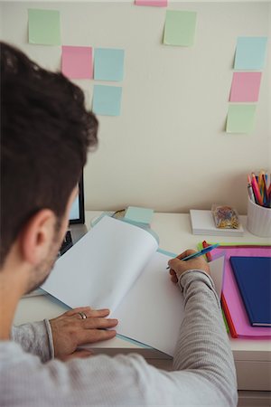 Rear view of man writing on document while sitting at desk Stock Photo - Premium Royalty-Free, Code: 6109-08944690