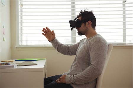 experiencing - Side view of man using virtual reality headset while sitting at desk Stock Photo - Premium Royalty-Free, Code: 6109-08944696