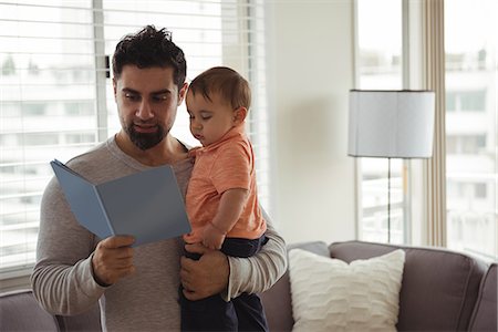 simsearch:6109-08537057,k - Father reading a book while holding his baby at home Stock Photo - Premium Royalty-Free, Code: 6109-08944703