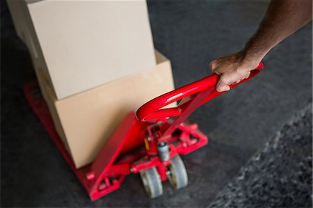 Cropped hand of worker pulling trolley loaded with boxes in warehouse Foto de stock - Sin royalties Premium, Código: 6109-08945114