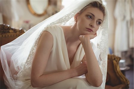 Thoughtful young bride in a white dress sitting on sofa in boutique Stock Photo - Premium Royalty-Free, Code: 6109-08945271