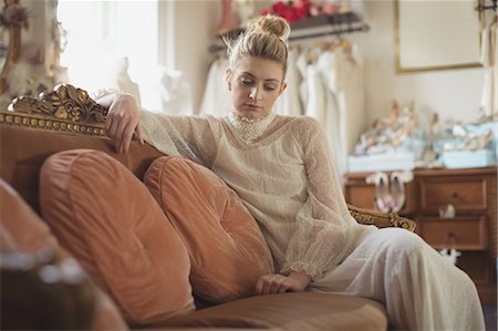 Thoughtful young bride in a white dress sitting on sofa in a boutique Stock Photo - Premium Royalty-Free, Code: 6109-08945286