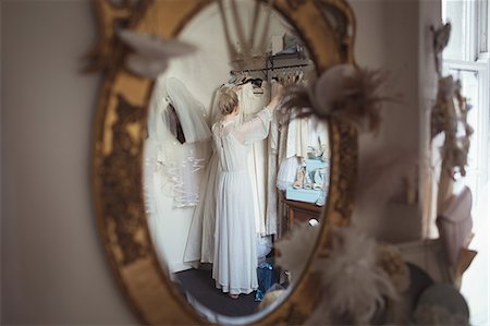 Reflection of bride selecting wedding dress from clothes hanger in the mirror at boutique Foto de stock - Sin royalties Premium, Código: 6109-08945290