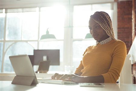 simsearch:6109-08945337,k - Female executive working on digital tablet at desk in office Fotografie stock - Premium Royalty-Free, Codice: 6109-08945348