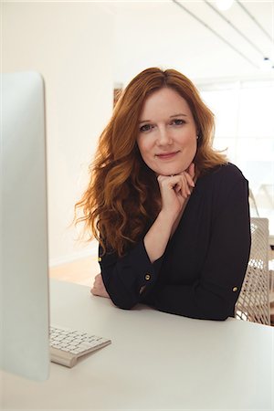 simsearch:6109-08945337,k - Portrait of female executive sitting at desk in office Fotografie stock - Premium Royalty-Free, Codice: 6109-08945323