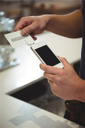 Cropped image of barista swiping credit card into device that is connected to mobile phone at cafe Foto de stock - Sin royalties Premium, Código: 6109-08945406