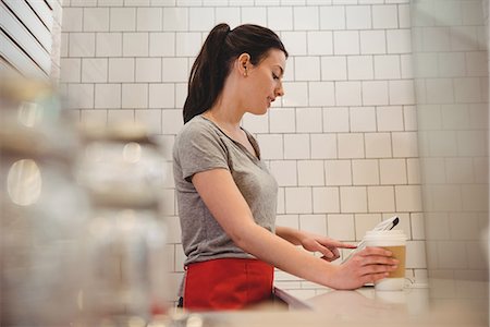 Side view of female barista holding coffee cup while using tablet PC in coffee shop Stock Photo - Premium Royalty-Free, Code: 6109-08945424