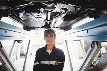 simsearch:6109-08952663,k - Female mechanic standing with arms crossed under a car Foto de stock - Sin royalties Premium, Código: 6109-08952675