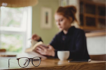 simsearch:6109-07496970,k - Woman sitting by dining table and reading a book Fotografie stock - Premium Royalty-Free, Codice: 6109-08952810