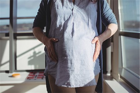 simsearch:6109-08764905,k - Mid section of pregnant woman standing near window in living room Photographie de stock - Premium Libres de Droits, Code: 6109-08953287