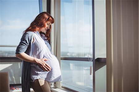 pensive woman glass - Thoughtful pregnant woman standing near window in living room Stock Photo - Premium Royalty-Free, Code: 6109-08953286